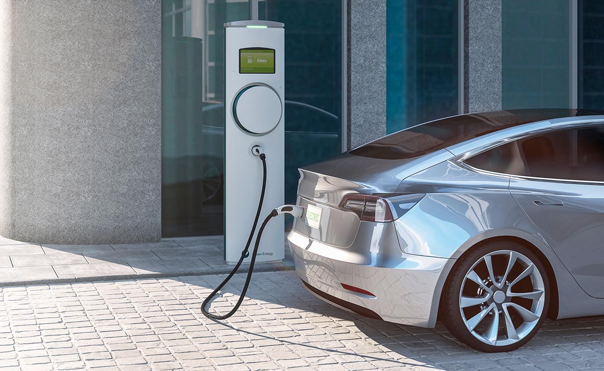 A grey electric vehicle plugged into a white retail EV charging station