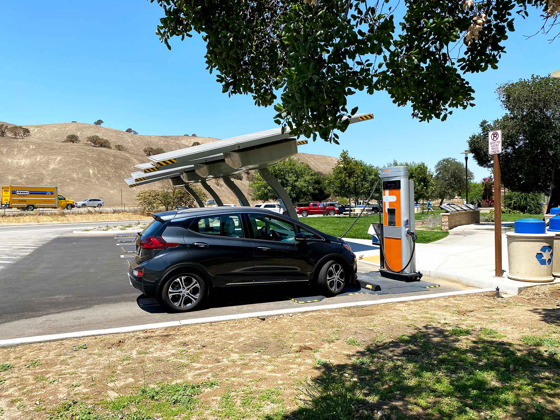 A black electric vehicle being charged at a park EV charging station