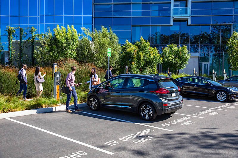 A man speaking to his colleague while charging his electric vehicle at his workplace EV charging station