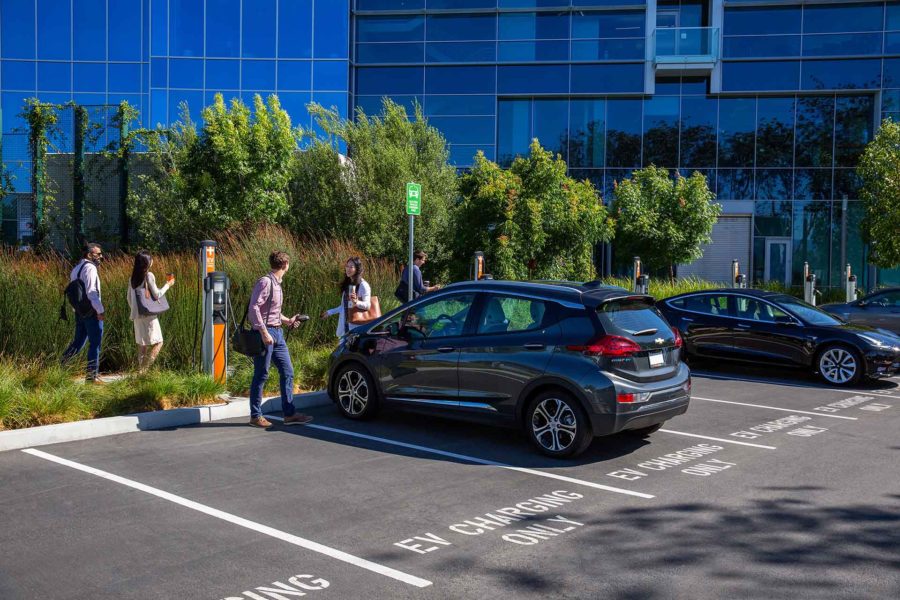 A man speaking to a friend while charging his electric vehicle at a retail EV charging station at his workplace